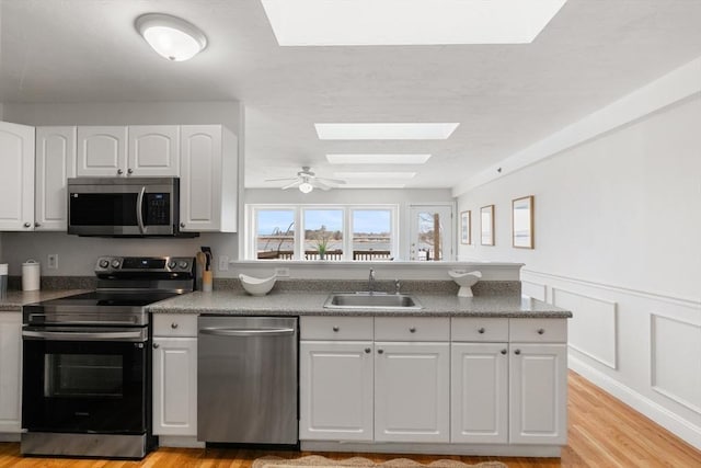 kitchen featuring a skylight, a sink, white cabinetry, appliances with stainless steel finishes, and dark countertops