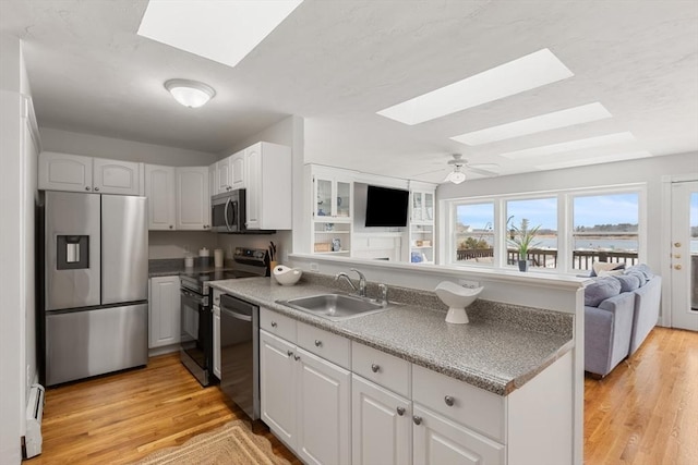 kitchen with stainless steel appliances, a skylight, a sink, and white cabinets