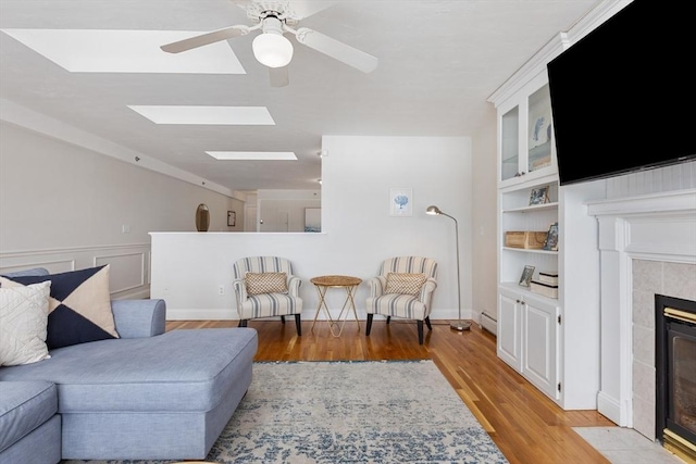 living area featuring light wood finished floors, built in features, a ceiling fan, a baseboard radiator, and a fireplace