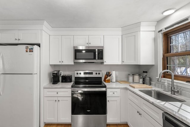 kitchen with stainless steel appliances, light stone counters, a sink, and white cabinets