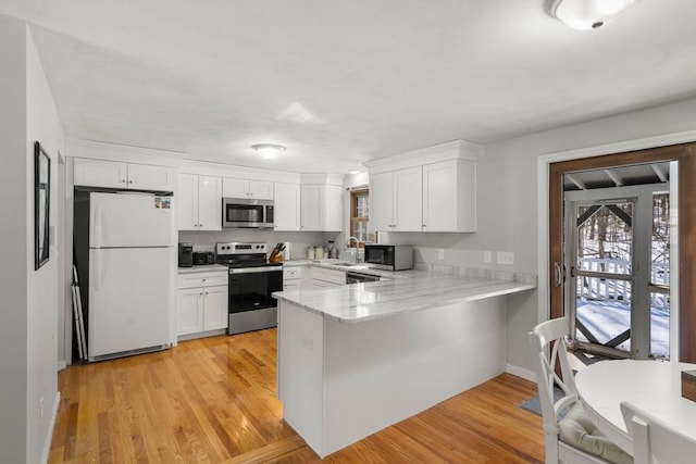 kitchen featuring stainless steel appliances, a peninsula, a sink, white cabinets, and light wood finished floors