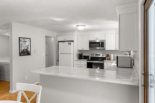 kitchen featuring white cabinets, light wood-style flooring, appliances with stainless steel finishes, a peninsula, and light stone countertops