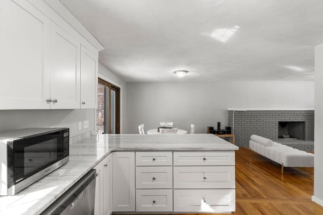 kitchen featuring white cabinets, stainless steel microwave, a peninsula, light stone countertops, and a fireplace