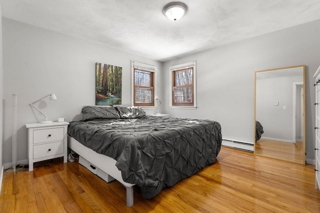 bedroom with light wood-style floors, baseboards, and baseboard heating