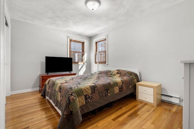 bedroom featuring a baseboard heating unit, light wood finished floors, and baseboards