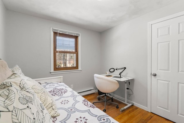 bedroom featuring a baseboard radiator, light wood-style flooring, and baseboards