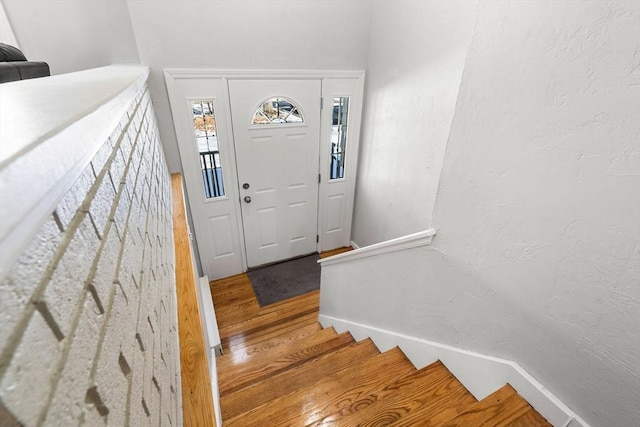 foyer featuring stairway, baseboards, wood finished floors, and a textured wall