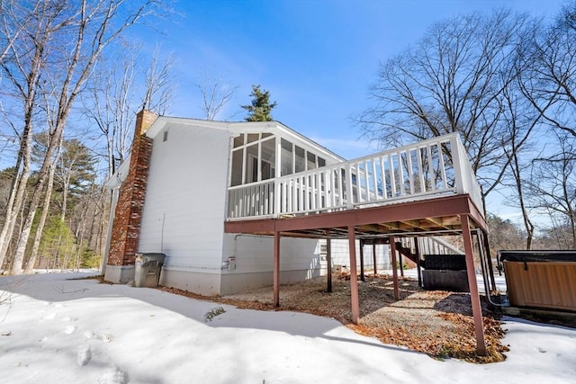 snow covered rear of property with a hot tub, a sunroom, a chimney, a deck, and a carport