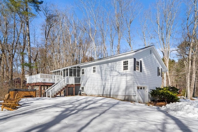 snow covered property with a hot tub, a sunroom, stairway, an attached garage, and a wooden deck