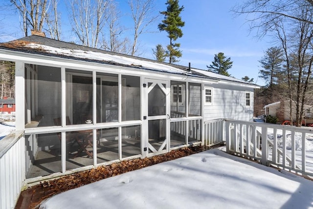 snow covered back of property featuring a sunroom and a chimney