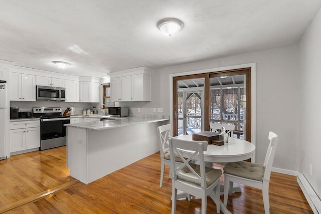 kitchen with stainless steel appliances, a baseboard radiator, a peninsula, and white cabinetry