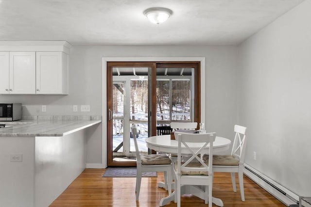 dining area with baseboards, light wood finished floors, and baseboard heating