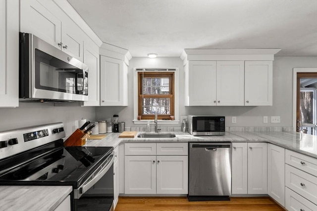 kitchen featuring light wood-style flooring, appliances with stainless steel finishes, white cabinetry, a sink, and light stone countertops