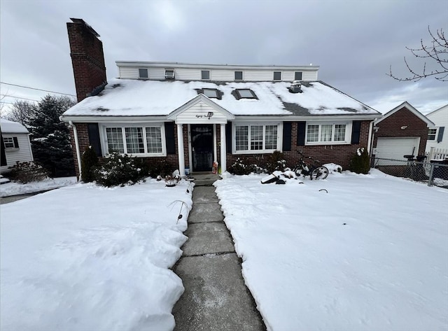 view of front facade featuring brick siding, a detached garage, a chimney, and fence