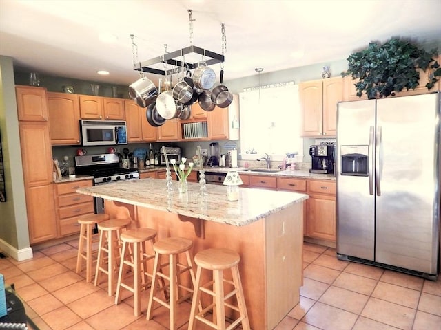 kitchen featuring a breakfast bar, sink, light tile patterned floors, a kitchen island, and stainless steel appliances