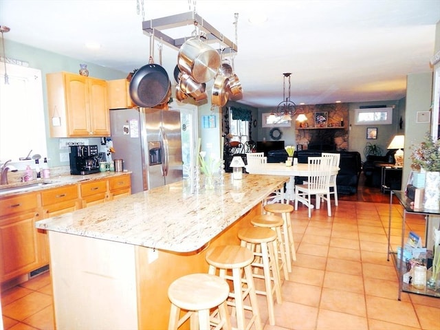 kitchen featuring sink, stainless steel fridge, a kitchen bar, a center island, and light tile patterned flooring