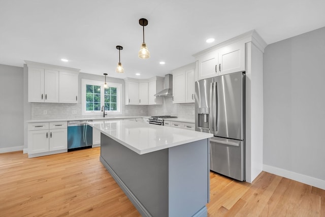 kitchen featuring stainless steel appliances, wall chimney exhaust hood, light hardwood / wood-style flooring, and white cabinets