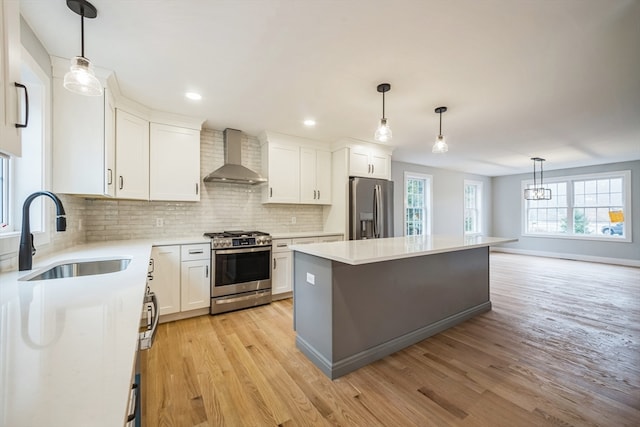 kitchen with wall chimney range hood, a kitchen island, white cabinetry, sink, and stainless steel appliances