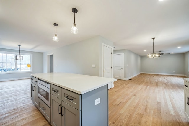 kitchen featuring gray cabinets, hanging light fixtures, stainless steel microwave, and light wood-type flooring