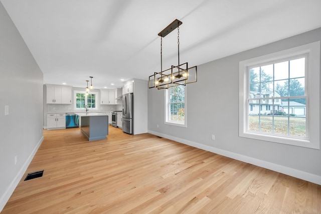 kitchen with appliances with stainless steel finishes, a center island, a healthy amount of sunlight, and decorative light fixtures