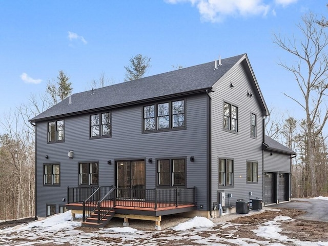 snow covered property with central AC, a shingled roof, a garage, a deck, and aphalt driveway