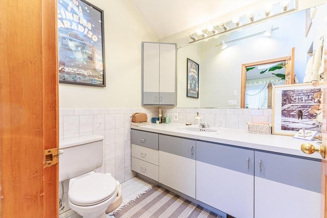 bathroom featuring tile patterned flooring, vaulted ceiling, toilet, vanity, and tile walls