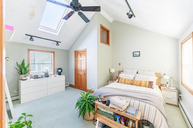 carpeted bedroom with multiple windows, track lighting, ceiling fan, and a baseboard heating unit