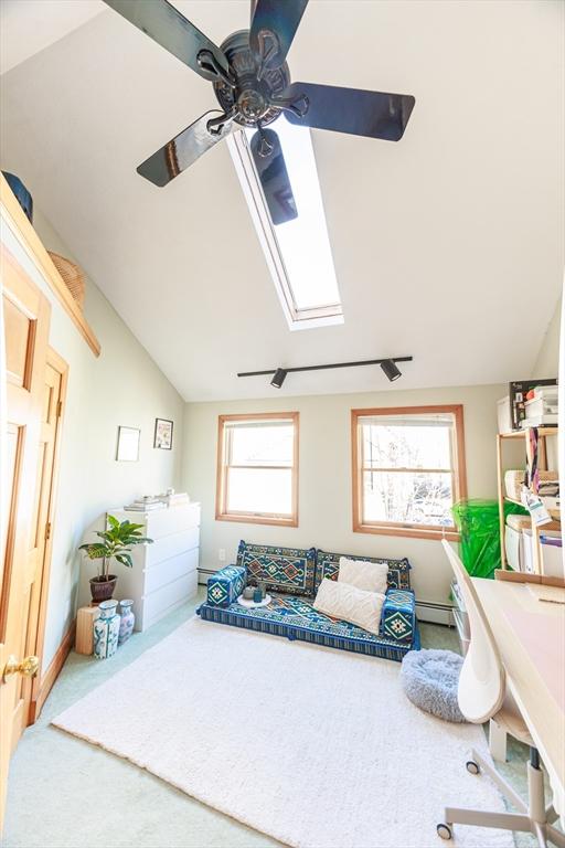 carpeted bedroom with ceiling fan, lofted ceiling with skylight, a baseboard radiator, and multiple windows