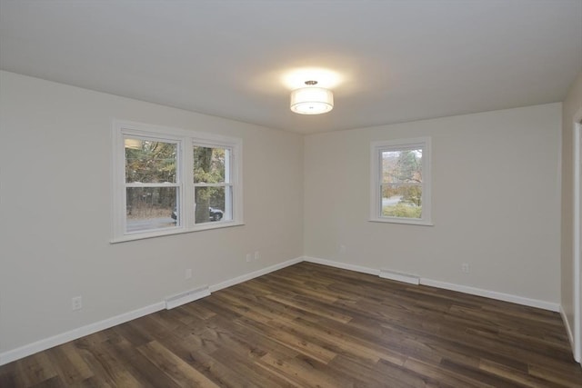 empty room featuring dark wood-style floors, visible vents, and baseboards