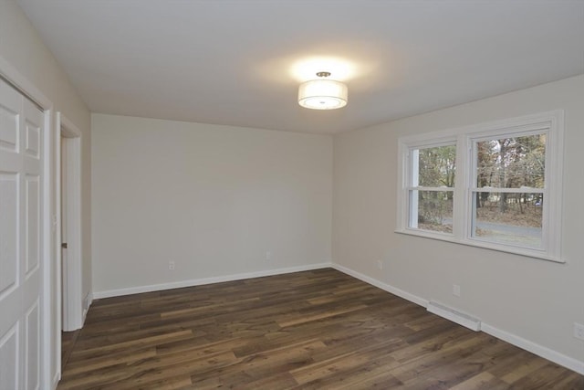 unfurnished room featuring baseboards, visible vents, and dark wood-type flooring