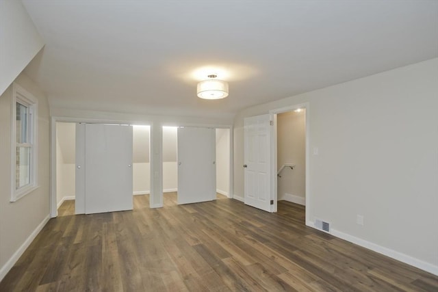 unfurnished bedroom featuring multiple closets, dark wood-style flooring, visible vents, and baseboards