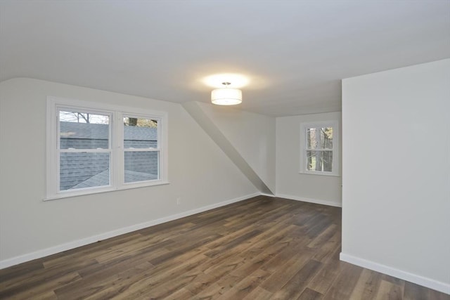 unfurnished room with dark wood-style floors, vaulted ceiling, plenty of natural light, and baseboards