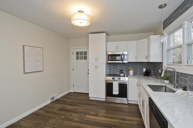 kitchen with light stone counters, stainless steel appliances, visible vents, dark wood-type flooring, and a sink