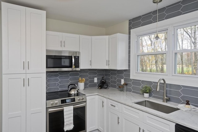 kitchen with appliances with stainless steel finishes, a sink, white cabinets, and tasteful backsplash