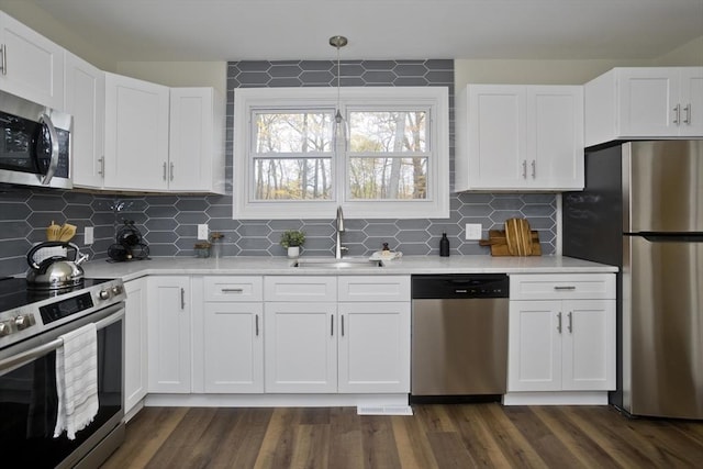 kitchen with appliances with stainless steel finishes, light countertops, a sink, and dark wood-style floors