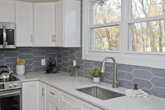 kitchen with stainless steel appliances, tasteful backsplash, a sink, and white cabinets