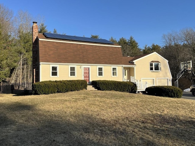 view of front facade with solar panels, fence, a gambrel roof, and a chimney