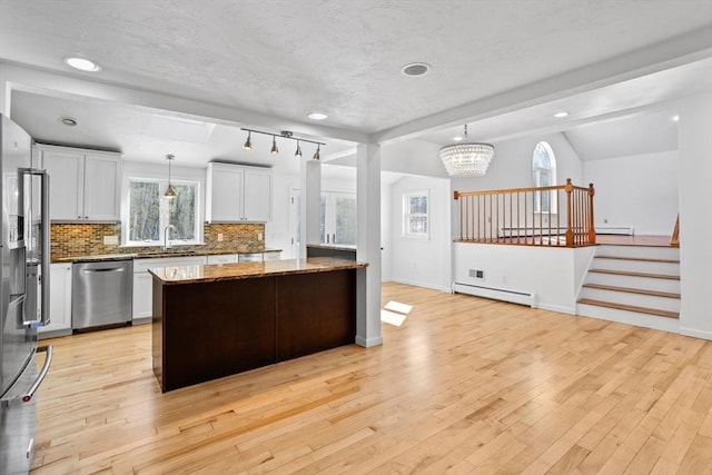 kitchen featuring dark stone countertops, a baseboard heating unit, tasteful backsplash, appliances with stainless steel finishes, and light wood finished floors