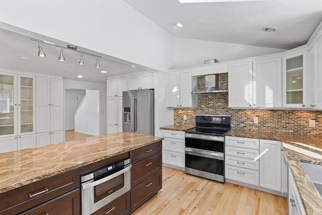 kitchen with wall chimney range hood, vaulted ceiling, light wood-style floors, white cabinets, and stainless steel appliances