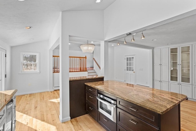 kitchen with oven, light wood-style flooring, light stone counters, lofted ceiling, and dark brown cabinets