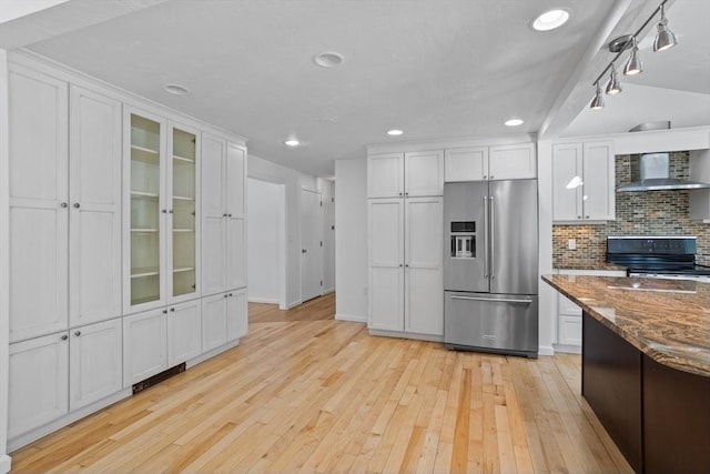 kitchen featuring light wood finished floors, backsplash, stainless steel appliances, white cabinetry, and wall chimney exhaust hood