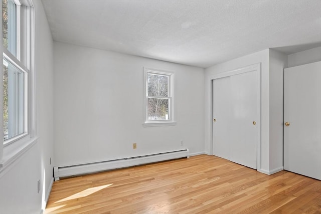 unfurnished bedroom with light wood finished floors, a textured ceiling, a baseboard heating unit, and a closet