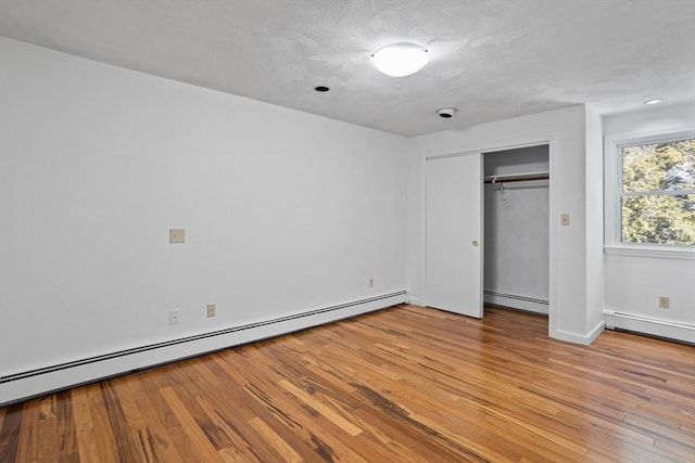 unfurnished bedroom featuring a baseboard heating unit, baseboards, light wood-type flooring, a closet, and a baseboard radiator