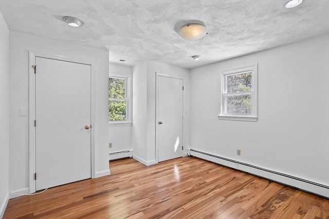 unfurnished bedroom with a baseboard radiator, baseboards, light wood-style floors, and a textured ceiling