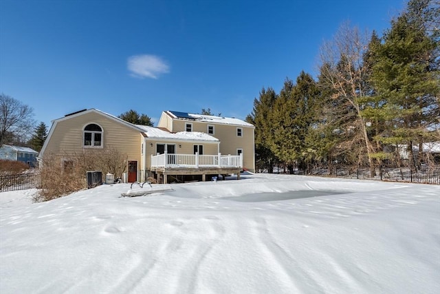 snow covered house with a deck, fence, and roof mounted solar panels