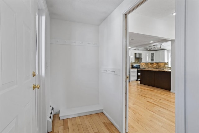 hallway with light wood finished floors and a baseboard radiator