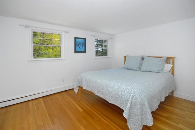 bedroom with baseboards, a baseboard heating unit, multiple windows, and wood finished floors