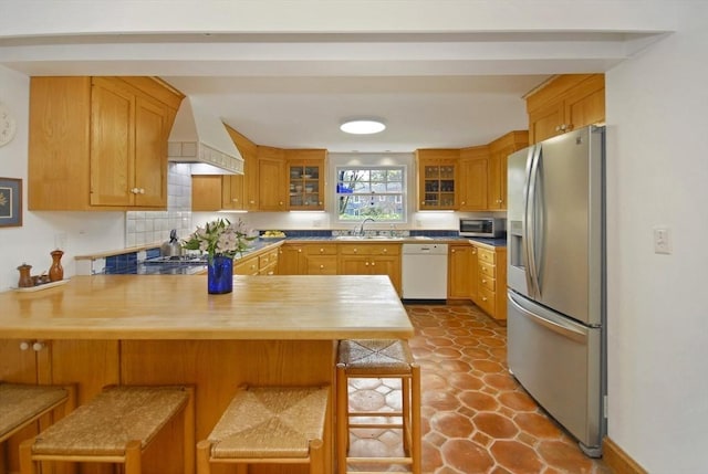 kitchen with a peninsula, custom exhaust hood, glass insert cabinets, a sink, and appliances with stainless steel finishes