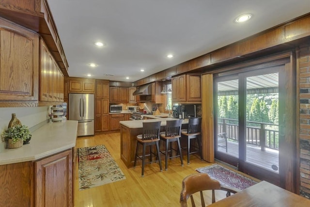 198 Mountain View Dr, Holyoke, MA 01040 - kitchen featuring appliances with stainless steel finishes, wall chimney exhaust hood, a peninsula, light wood finished floors, and brown cabinetry
