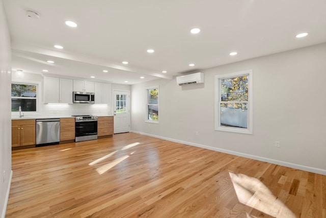 kitchen featuring sink, an AC wall unit, light hardwood / wood-style floors, white cabinets, and appliances with stainless steel finishes